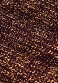 Close-up van gestructureerde breistof met doorweven metalen gouden en donkerpaarse draden die een verhoogd, geordend oppervlak creëren.