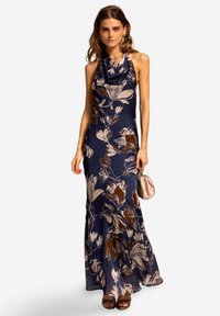 Marineblauer Floral-Halter-Abendkleid mit drapierter Halslinie, das große cremefarbene und braune Blumenmuster aufweist und eine figurbetonte Silhouette hat. Ergänzt durch eine kleine Clutch.