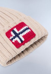 Berretto lavorato a maglia beige con una texture a coste, caratterizzato da un evidente patch rosso con un design norvegese a croce blu e bianca.