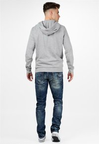 Hoodie gris et jeans en denim bleu. Le hoodie a un cordon de serrage et une poche kangourou. Les jeans présentent un délavage vieilli et des poches arrière avec des détails de couture.