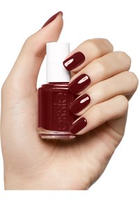 Bottiglia di smalto per unghie borgogna con un tappo bianco tenuta in una mano, con unghie lucide e curate dello stesso colore.