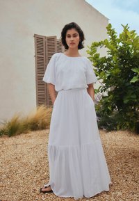 Vestido largo blanco con mangas cortas abullonadas, cintura entallada y bajo con volantes. Hecho de tela ligera, presenta una silueta relajada.