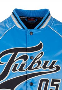 Veste universitaire bleue avec col côtelé, boutons-pression, inscription "Fubu" en noir et blanc, et numéro "05" sur le devant.