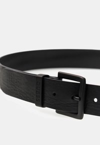 Cintura in pelle nera con una texture liscia, dotata di una fibbia in metallo nero opaco e logo del marchio in rilievo. Regolabile con più perforazioni.