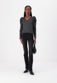 Black puff-sleeve top with a V-neck, made of textured knit material. Paired with fitted black jeans and pointed toe heels.