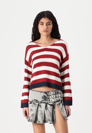 Rød og hvit stripete cropped genser med v-hals og marineblå kant, kombinert med et grått denimskjørt med folder og knappedetaljer.