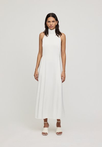 Witte mouwloze maxi-jurk met een hoge halslijn, een gladde textuur en een ontspannen pasvorm; gecombineerd met lichte, open-teensandalen.