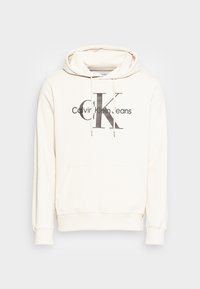 Sudadera de color beige claro hecha de algodón con un bolsillo delantero tipo canguro. Cuenta con capucha ajustable y un gran logo impreso "CK" y "Calvin Klein Jeans".