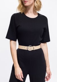 Mujer que lleva un conjunto de pantalones y top de manga corta negro acanalado con un cinturón beige que tiene una hebilla ovalada plateada.