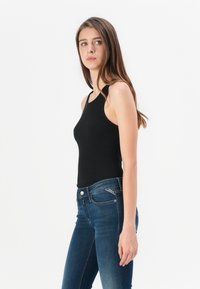 Svart ribbestrikket tanktopp med en tettsittende design og smale stropper, kombinert med mørkeblå skinny jeans med en klassisk fem-lommers design.