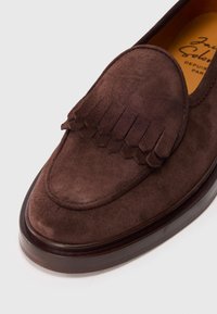 Brązowe zamszowe mokasyny z frędzlami na przodzie, zaokrąglonym czubkiem oraz elegancką skórzaną podeszwą. Bogata tekstura i elegancki design.