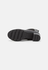 Bottine en cuir noir avec une finition texturée, semelle en caoutchouc robuste dotée de rainures profondes pour une traction optimale et un léger talon.