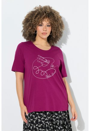 Kvinde med krøllet hår iført en lilla t-shirt med en hvid kontinuerlig linje håndtegning og et sort-hvidt mønstret nederdel.