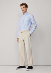 Camisa azul claro de botones, pantalones beige con cinturilla elástica y zapatillas negras. Diseño clásico con un bolsillo en la camisa.