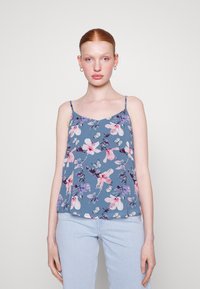 Camiseta sin mangas floral de tela azul con patrones en rosa y púrpura. Presenta tirantes finos y un corte holgado, combinada con jeans azul claro.
