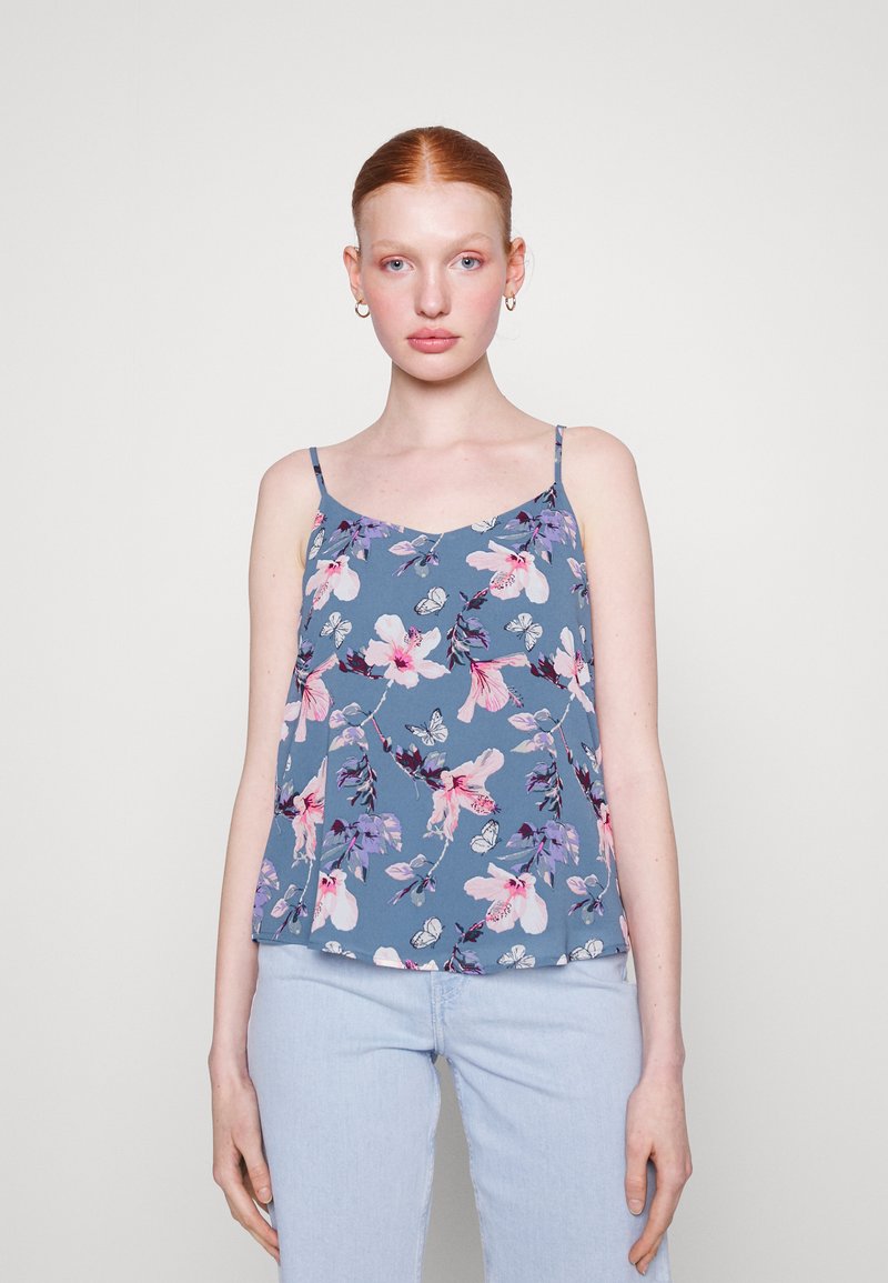 Blomstermønstret cami-topp i blått stoff med rosa og lilla mønster. Har tynne stropper og en avslappet passform, stylet med lyseblå jeans.