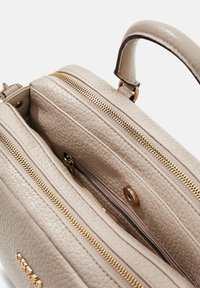 Beige leren handtas met textuur, voorzien van twee ritsvakken, een zak met magneetsluiting en een stevige handgreep aan de bovenkant.