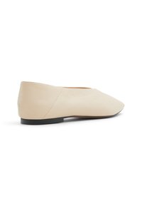 Ballerines en cuir beige avec un bout pointu et une semelle noire basse. La surface est lisse, mettant en avant des coutures minimales et un design épuré.