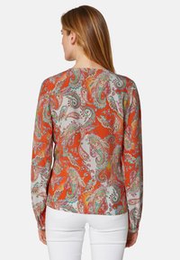 Langärmlige Bluse mit einem lebhaften orangen Paisleymuster und grünen sowie pinken Akzenten, aus leichtem Stoff und mit rundem Ausschnitt.