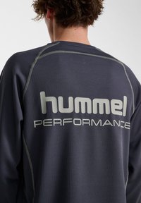 Marineblaue Langarm-Performance-Shirts aus strukturiertem Material, mit reflektierenden Nähten und großem weißen "hummel PERFORMANCE"-Logo auf dem Rücken.