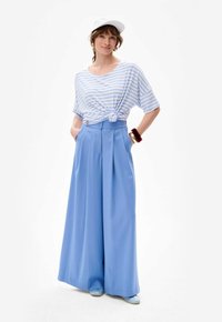 Lichtblauwe geplooide wijde broek gecombineerd met een geknoopte wit-blauwe gestreepte t-shirt, aangevuld met een witte pet en bijpassende schoenen.