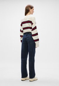 Pulover gros cu dungi roșii și bleumarin, purtat cu blugi închiși la culoare, cu talie înaltă. Adidași completează ținuta. Textură netedă, croială lejeră.