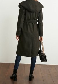 Lang mørk grå uldfrakke med hætte, bælte i taljen og en glat tekstur. Kombinationen med mørke jeans og sorte ankelstøvler. Bemærkelsesværdig detalje på håndtasken.