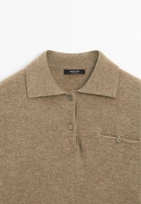 Polo en maille beige avec col, deux boutons sur le devant et une petite poche poitrine boutonnée, étiqueté Massimo Dutti.