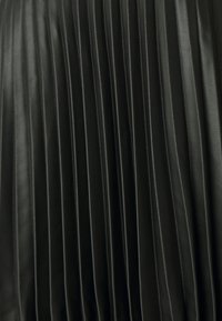 Tessuto in pelle nera con pieghe verticali, caratterizzato da una texture liscia e lucida e da una brillantezza uniforme su tutto il materiale.