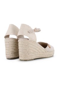 Sandalias de cuña de esparto beige con suela de yute trenzado, correa de tobillo ajustable y parte superior de ante suave con un pequeño detalle metálico.
