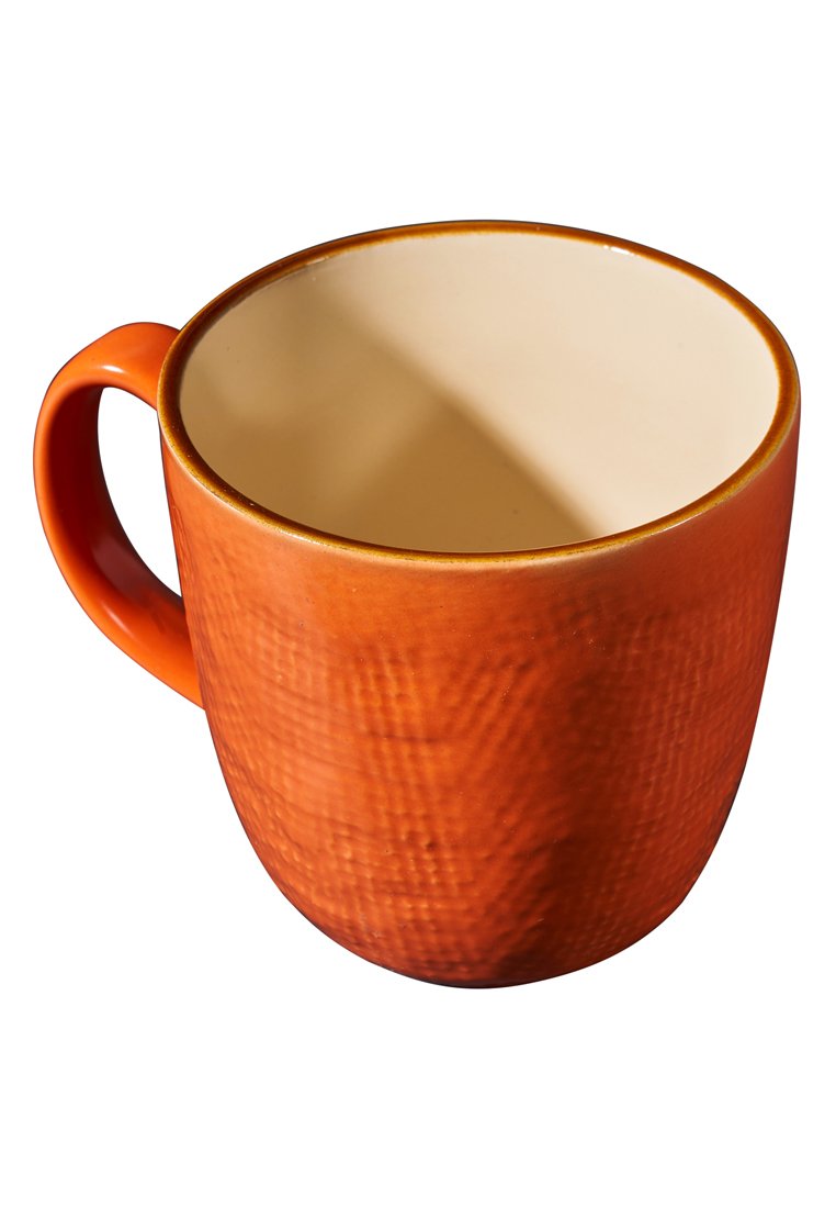 Pomarańczowy ceramiczny kubek o fakturowanej powierzchni z gładkim beżowym wnętrzem, prezentowany przechylony i pusty, z uchwytem po lewej stronie.