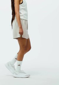 Světle šedé sportovní šortky a odpovídající tílko jsou kombinovány s bílými teniskami a ponožkami se třemi hnědými pruhy. Jednoduché pozadí.