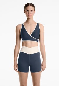 Marin aktivklädesset som har en omslags-topp med krämfärgade detaljer och högmidjade shorts. Slät, elastisk tyg med modern design.
