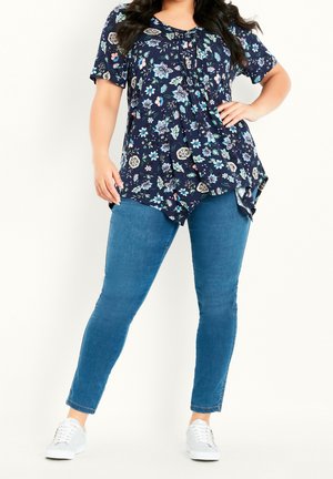 Top con stampa floreale su sfondo blu navy, maniche corte e frontale plissettato. Abbinato a jeans blu aderenti e sneakers bianche.