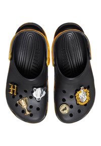 Schwarze Holzschuhe mit gelben Akzenten, verziert mit dekorativen Pins: ein Dachs, eine Tasse und ein Hausemblem. Belüftungslöcher an der Oberseite.