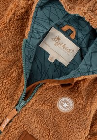 Giacca per bambini marrone e pelosa con zip teal e fodera a fantasia, dotata di un'etichetta e di un patch del logo del marchio sul petto.