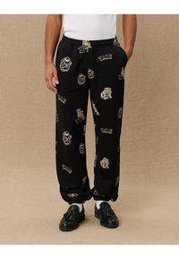 Zwarte sweatpants met elastische boorden, voorzien van beige Yale-logo's en bulldogafbeeldingen over het geheel. Gemaakt van zachte stof, ontworpen voor comfort.