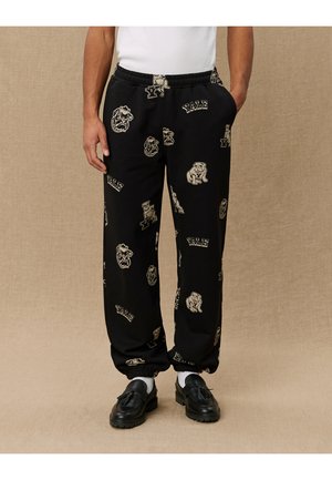 Black sweatpants with elastic cuffs, featuring beige Yale logos and bulldog graphics throughout. Made of soft fabric, designed for comfort.