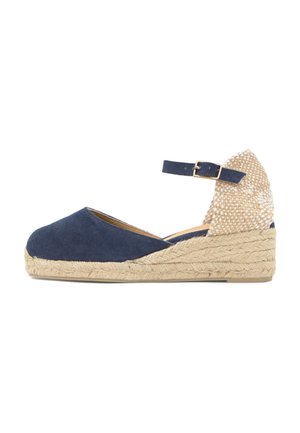 Alpargata de cuña azul marino con suela trenzada de yute, tacón beige texturizado y tira ajustable en el tobillo con hebilla dorada.