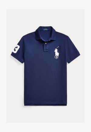 Jūras spēku polo krekls, izgatavots no kokvilnas. Tam ir divu pogu aizdare, īsas piedurknes un balts izšūts logo uz krūtīm un piedurknes.