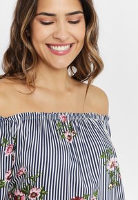 Ribbad off-shoulder-topp med marinblå och vita ränder, prydd med blommig brodyr i rosa och grönt fram. Slen tygkänsla.