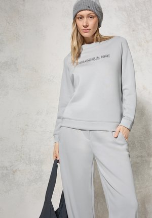 Light gray sweatshirt with "Colorful Life" text design, paired with matching gray pants. Material appears soft, featuring a relaxed fit and crew neckline.