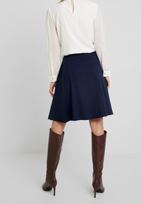 Marinblå utsvängd kjol av mjukt tyg, tillsammans med en vit blus med genomskinliga ärmar och detaljer med nyckelhål i ryggen. Bruna knähöga stövlar.