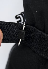 Cinghietta di stoffa nera con chiusura a strappo, dettaglio in metallo a forma di anello e una superficie liscia, che mette in mostra le cuciture su uno sfondo semplice.