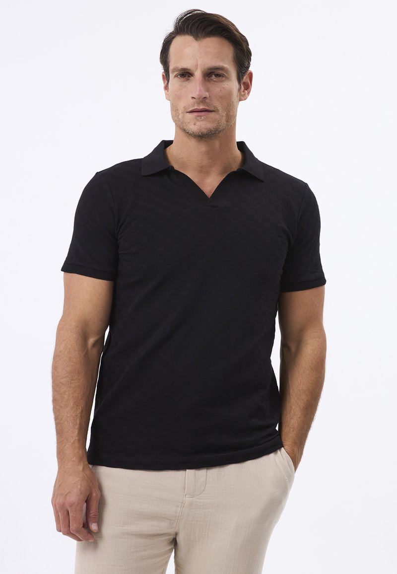 Polo noir texturé avec un col en V et des manches courtes, associé à un pantalon de couleur claire. Présente des détails de motif subtils.
