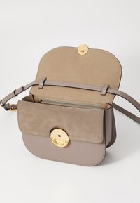Borsa in pelle grigio chiaro con chiusura circolare dorata, pattina in morbido camoscio e tracolla regolabile; l'interno presenta una tasca con zip e foderatura liscia.