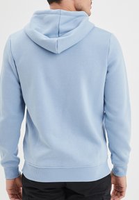 Felpa di un blu chiaro con una vestibilità rilassata, dotata di cappuccio con coulisse e polsini e orlo a coste. Tessuto morbido e dettagli di cucitura minimi.