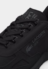Baskets Lacoste noires avec des lacets noirs, texte de marque et logo crocodile sur le côté et la languette en vue rapprochée.