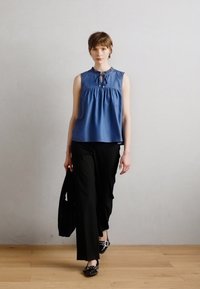 Μπλε αμάνικο μπλουζάκι με συγκεντρωμένη μέση και λεπτομέρεια δέσμης, συνδυασμένο με μαύρες παντελόνες καμπάνα και μαύρες πατούσες με σχέδιο.