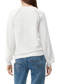 White sweatshirt with a round neckline, textured details on raglan seams, and elasticated hems, paired with blue high-waisted denim jeans.